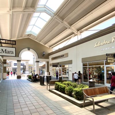 Shoppers walk through the open-air corridor of San Francisco Premium Outlets, lined with luxury storefronts.
